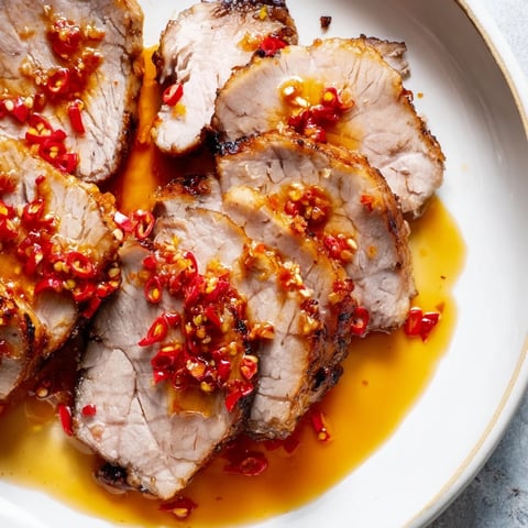 Golden-brown Bavarian roast pork, expertly sliced, with a vibrant chili-ginger sauce drizzled over each piece.