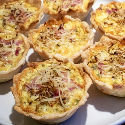 Golden baked mini quiches artfully arranged on a holiday board, garnished and ready to serve.