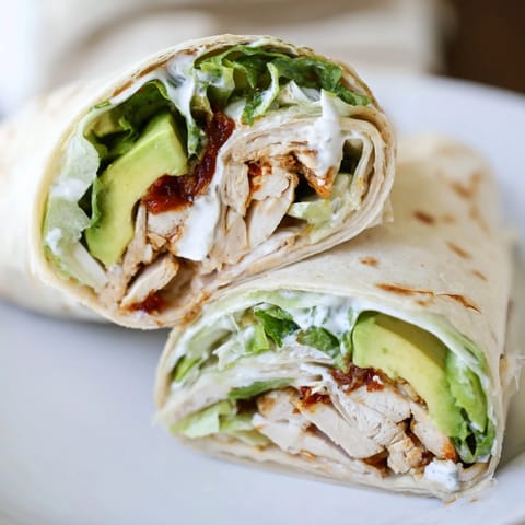 Ein frisch zubereiteter Smoky Chipotle Chicken Wrap gefüllt mit knusprigem Salat, Zwiebeln und würziger Joghurt-Sauce auf dem Teller