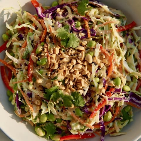 Crunchy Thai Peanut Salad topped with chopped peanuts, sesame seeds, and lime wedges, perfect for a light vegetarian meal.
