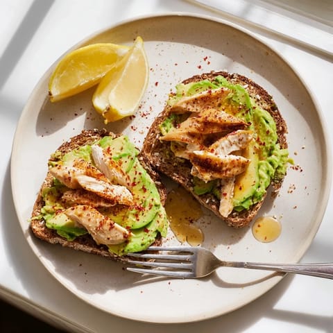 Frisch vom Grill: würziges Hähnchen auf cremig geröstetem Avocado-Toast, verfeinert mit Chiliflocken für eine scharfe Note.