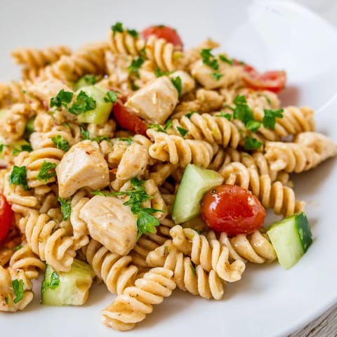 Zwei Schüsseln Honey Mustard Chicken Pasta Salad, eine mit gekochtem Hähnchen und die andere mit Tofu, beide mit knusprigem grünem Salat garniert und in Sandstein-Umgebung stilvoll präsentiert.