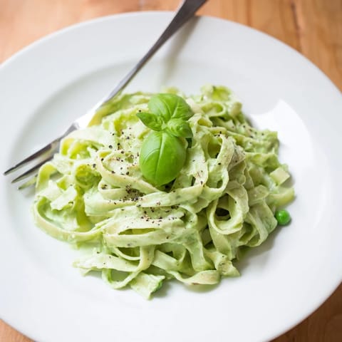 Creamy Green Pea Alfredo served over fettuccine, garnished with fresh basil and cracked black pepper.