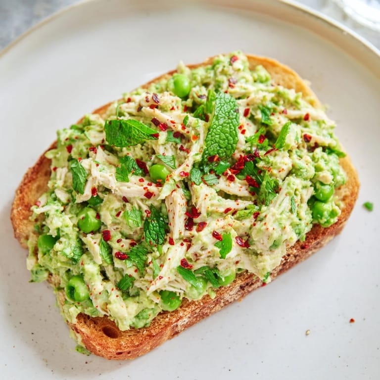 Smashed pea and chicken toast with crumbled feta, mint, and lemon zest on rustic bread.