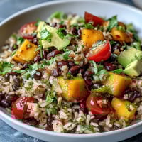 Bunter Schälchen mit braunem Reis, Mango und schwarzen Bohnen, verfeinert mit Limettendressing.  