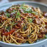 Bowl of Korean Turkey Fried Noodles with bouncy noodles, colorful veggies, and sesame garnish.